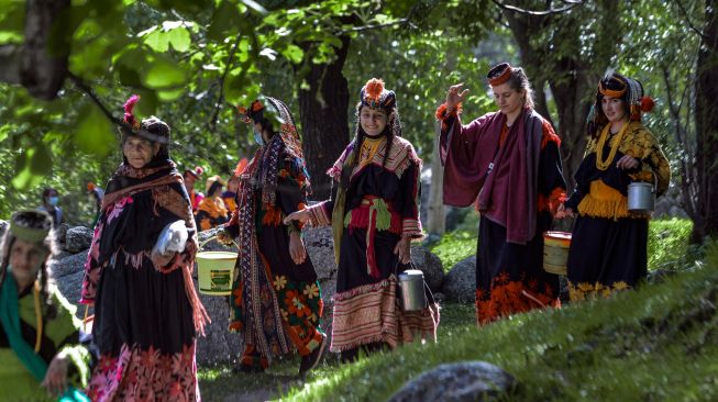 Wanita suku Kalash yang mengenakan pakaian tradisional berjalan menuju rumah kerabat mereka untuk mengumpulkan susu dan menari sebagai bagian dari ritual pada hari pertama festival 'Joshi' di desa Bumburet, Pakistan, Sabtu (14/5/2022). [Abdul MAJEED / AFP]