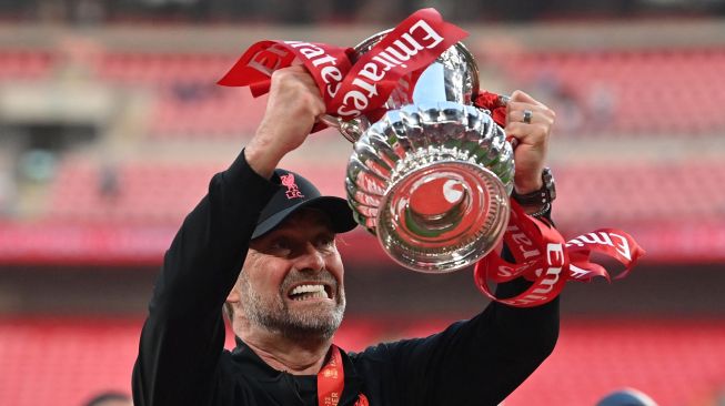 Manajer Liverpool Jurgen Klopp selebrasi dengan mengangkat trofi Piala FA setelah memenangkan pertandingan sepak bola final Piala FA Inggris antara Chelsea dan Liverpool di Stadion Wembley, London, Inggris (Sabtu 14/5/2022). [Glyn KIRK / AFP]