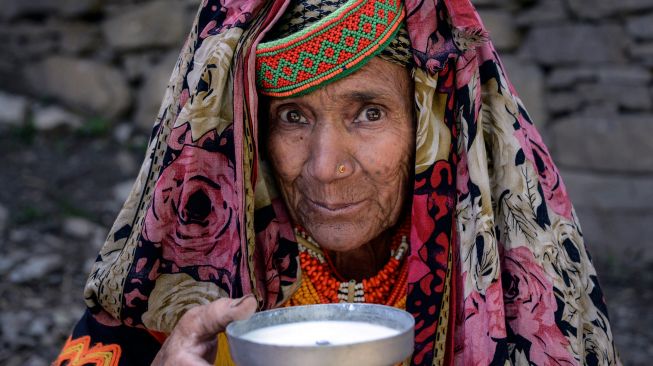 Seorang wanita suku Kalash yang mengenakan pakaian tradisional minum susu sebagai bagian dari ritual pada hari pertama festival 'Joshi' di desa Bumburet, Pakistan, Sabtu (14/5/2022). [Abdul MAJEED / AFP]
