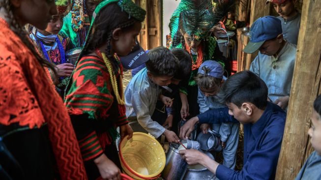 Wanita suku Kalash yang mengenakan pakaian tradisional mengumpulkan susu dari rumah kerabat mereka sebagai bagian dari ritual pada hari pertama festival 'Joshi' di desa Bumburet, Pakistan, Sabtu (14/5/2022). [Abdul MAJEED / AFP]
