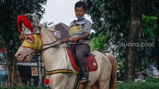 Seorang anak berwisata sambil menunggangi kuda di kawasan Kanal Banjir Timur (KBT), Jakarta Timur, Senin (16/5/2022). [Suara.com/Alfian Winanto] 