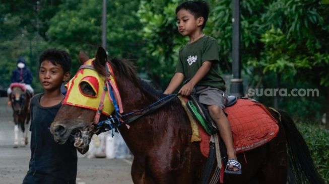 Seorang anak berwisata sambil menunggangi kuda di kawasan Kanal Banjir Timur (KBT), Jakarta Timur, Senin (16/5/2022). [Suara.com/Alfian Winanto] 