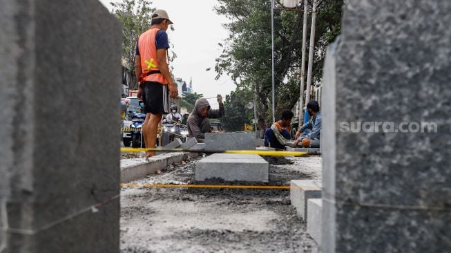 Pekerja menyelesaikan proyek revitalisasi jalur pedestrian di kawasan Kota Tua, Jakarta Barat, Kamis (19/5/2022). [Suara.com/Alfian Winanto]