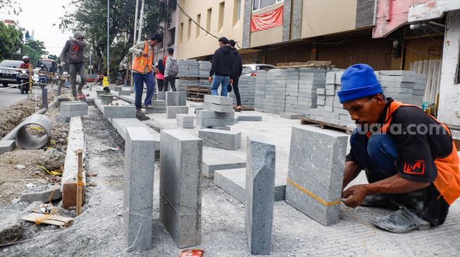 Pekerja menyelesaikan proyek revitalisasi jalur pedestrian di kawasan Kota Tua, Jakarta Barat, Kamis (19/5/2022). [Suara.com/Alfian Winanto]