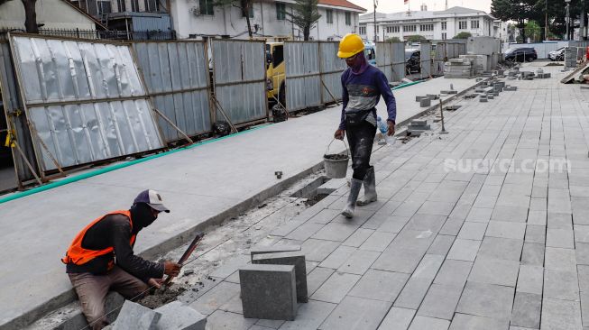 Pekerja menyelesaikan proyek revitalisasi jalur pedestrian di kawasan Kota Tua, Jakarta Barat, Kamis (19/5/2022). [Suara.com/Alfian Winanto]