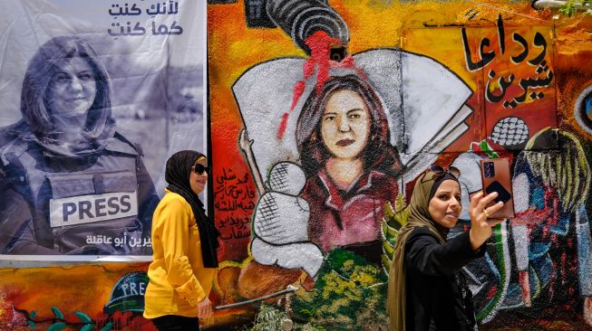 Dua wanita berswafoto di sebuah pameran seni yang digelar untuk menghormati mendiang jurnalis Al-Jazeera Palestina, Shireen Abu Akleh di kota Jenin, Palestina, Kamis (19/5/2022). [RONALDO SCHEMIDT / AFP]