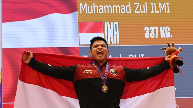 Lifter Indonesia Muhammad Zul Ilmi membawa bendera Merah Putih usai pengalungan medali nomor 89 kilogram angkat berat SEA Games 2021 Vietnam di Hanoi Sports Training Centre, Hanoi, Vietnam, Minggu (22/5/2022). ANTARA FOTO/Aditya Pradana Putra
