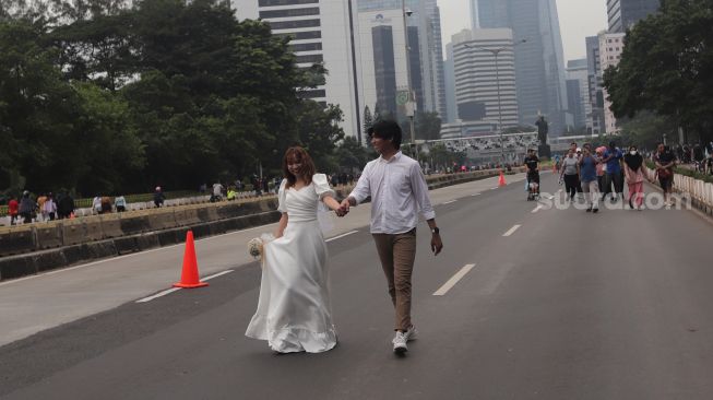 Warga melakukan sesi foto 'prewedding' di area 'car free day' (CFD) di Jalan Jenderal Sudirman, Jakarta, Minggu (22/5/2022). [Suara.com/Angga Budhiyanto]