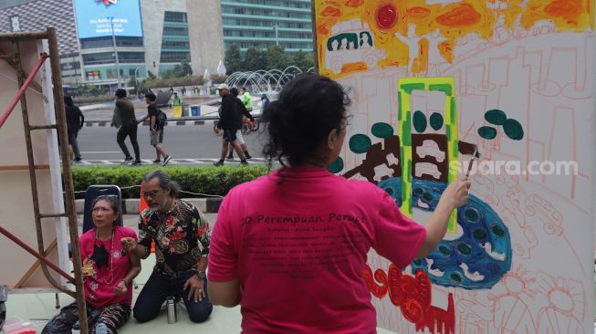 Seniman yang tergabung dalam Perempuan Perupa Indonesia melukis dan menggelar pameran bersama di depan Pos Polisi Thamrin, Jakarta, Minggu (22/5/2022). [Suara.com/Angga Budhiyanto]