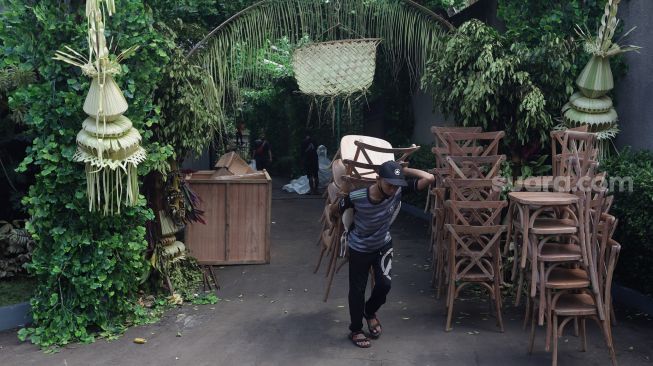 Pekerja membawa bangku saat membongkar dekorasi pernikahan di kediaman Maudy Ayunda di kawasan Cilandak, Jakarta, Senin (23/5/2022). [Suara.com/Angga Budhiyanto]