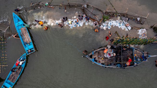 Foto udara personel kepolisian dari Polsek Kesatuan Pelaksanaan Pengamanan Pelabuhan (KP3) Tanjung Emas Semarang bersama warga dan relawan bergotong royong menutup tembok kawasan industri atau tanggul yang jebol dengan konstruksi pagar bambu dan karung berisi pasir dan batu di kawasan industri Pelabuhan Tanjung Emas Semarang, Jawa Tengah, Rabu (25/5/2022).  ANTARA FOTO/Aji Styawan