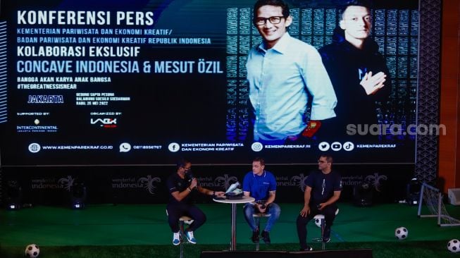 Pesepakbola Mesut Ozil (tengah) bersama Menteri Pariwisata, Ekonomi dan Kreatif (Meparekraf) Sandiaga Uno saat hadir dalam konferensi pers di Kementerian Pariwisata, Ekonomi dan Kreatif (Kemenparekraf), Jakarta Pusat, Rabu (25/5/2022). [Suara.com/Alfian Winanto]