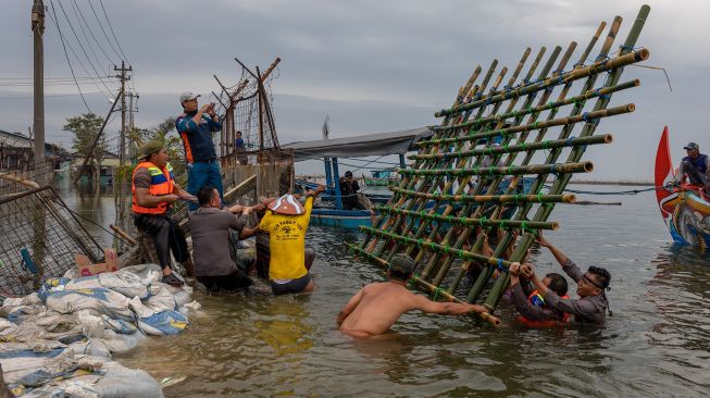 Personel kepolisian dari Polsek Kesatuan Pelaksanaan Pengamanan Pelabuhan (KP3) Tanjung Emas Semarang bersama warga dan relawan bergotong royong menutup tembok kawasan industri atau tanggul yang jebol dengan konstruksi pagar bambu dan karung berisi pasir dan batu di kawasan industri Pelabuhan Tanjung Emas Semarang, Jawa Tengah, Rabu (25/5/2022).  ANTARA FOTO/Aji Styawan