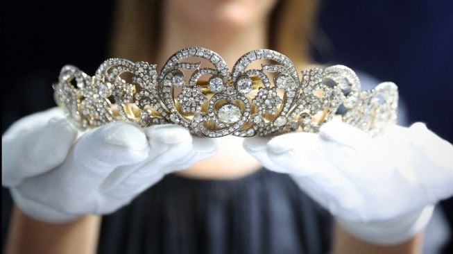 Seorang karyawan Sotheby mengangkat mahkota 'Spencer Tiara' yang dikenakan oleh Putri Diana pada hari pernikahannya pada tahun 1981 saat sesi pemotretan untuk mempromosikan Sotheby's Jubilee Season, di London, Inggris, Jumat (27/5/2022). [ADRIAN DENNIS / AFP]