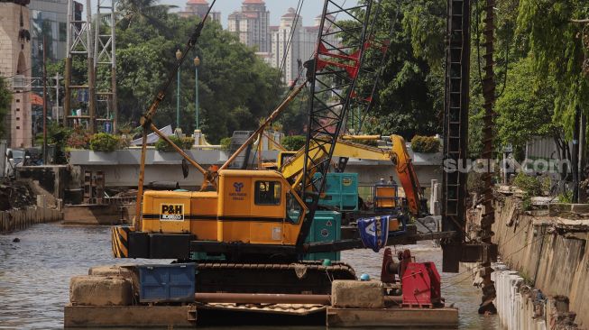 Pekerja dibantu alat berat menyelesaikan pembangunan turap anak Kali Ciliwung di kawasan Pasar Baru, Jakarta, Minggu (29/5/2022). [Suara.com/Angga Budhiyanto]