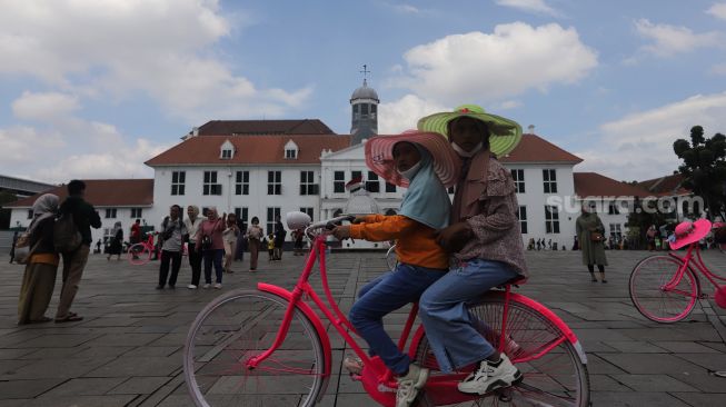 Warga menaiki sepeda saat berwisata di Taman Fatahillah, Kota Tua, Jakarta, Minggu (29/5/2022). [Suara.com/Angga Budhiyanto]