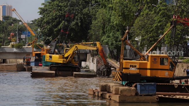 Pekerja dibantu alat berat menyelesaikan pembangunan turap anak kali Cilwung di kawasan Pasar Baru, Jakarta, Minggu (29/5/2022). [Suara.com/Angga Budhiyanto]