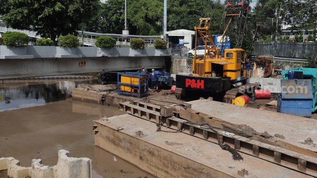 Pekerja dibantu alat berat menyelesaikan pembangunan turap anak Kali Ciliwung di kawasan Pasar Baru, Jakarta, Minggu (29/5/2022). [Suara.com/Angga Budhiyanto]