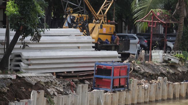 Pekerja beristirahat di sela menyelesaikan pembangunan turap anak Kali Ciliwung di kawasan Pasar Baru, Jakarta, Minggu (29/5/2022). [Suara.com/Angga Budhiyanto]