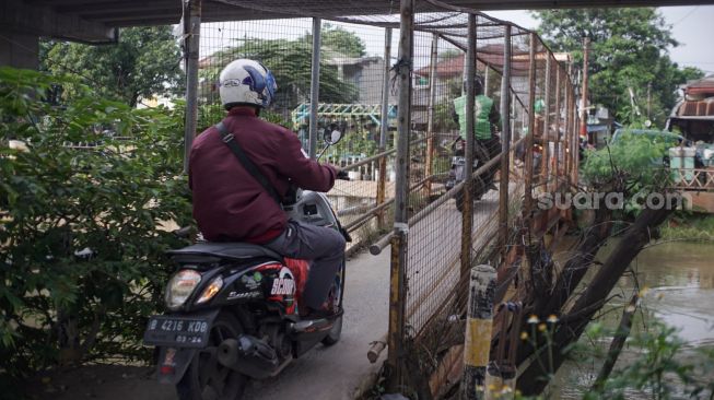 Pengendara motor melintasi Jembatan Penyebrangan Orang (JPO) di atas sungai Kalimalang di Jl. KH. Noer Ali, Kalimalang, Jakarta Timur, Kamis (2/6/2022). [Suara.com/Alfian Winanto]