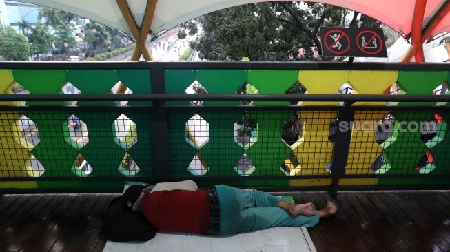 Warga tertidur di jembatan penyeberangan orang (JPO) di kawasan Pasar Minggu, Jakarta, Kamis (2/6/2022). [Suara.com/Angga Budhiyanto]