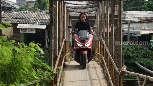 Pengendara motor melintasi Jembatan Penyebrangan Orang (JPO) di atas sungai Kalimalang di Jl. KH. Noer Ali, Kalimalang, Jakarta Timur, Kamis (2/6/2022). [Suara.com/Alfian Winanto]