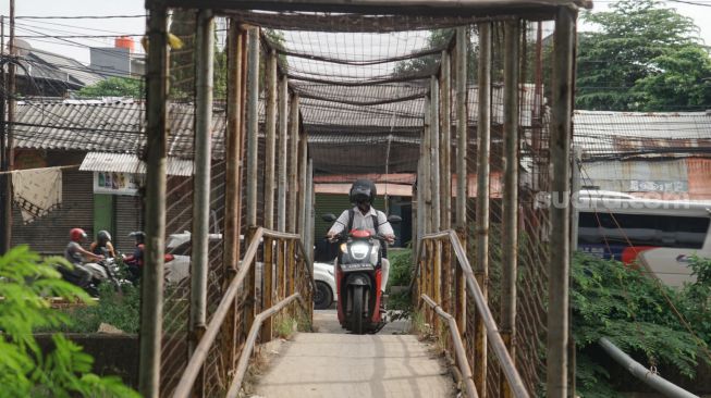 Pengendara motor melintasi Jembatan Penyebrangan Orang (JPO) di atas sungai Kalimalang di Jl. KH. Noer Ali, Kalimalang, Jakarta Timur, Kamis (2/6/2022). [Suara.com/Alfian Winanto]