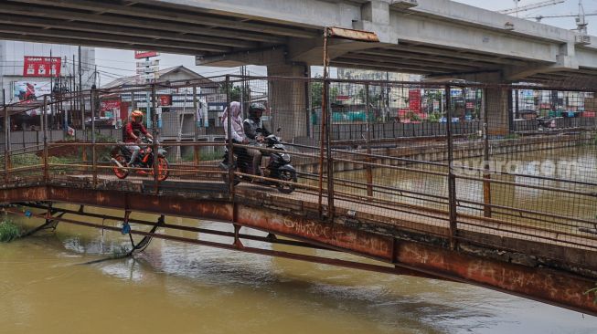 Pengendara motor melintasi Jembatan Penyebrangan Orang (JPO) di atas sungai Kalimalang di Jl. KH. Noer Ali, Kalimalang, Jakarta Timur, Kamis (2/6/2022). [Suara.com/Alfian Winanto]