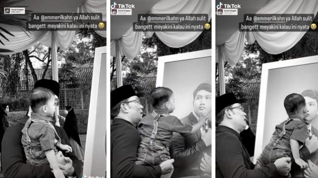 Momen haru Ridwan Kamil menggendong anak angkatnya, Arkana Aidan Misbach, yang kemudian tampak mengelus dan mencium foto Emmeril Kahn Mumtadz. (Twitter/@AREAJULID)