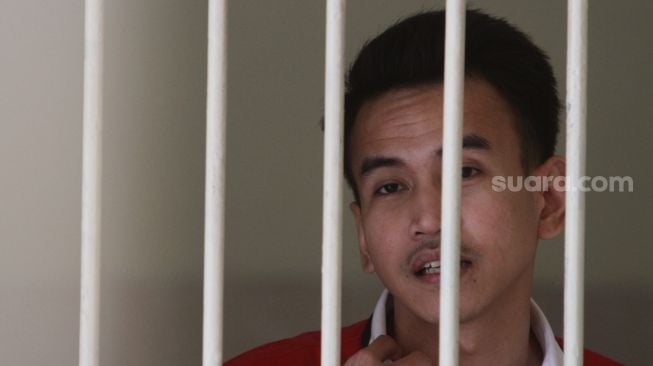 Terdakwa kasus pelanggaran Undang-Undang (UU) ITE Adam Deni menjawab pertanyaan awak media dari ruang tahanan Pengadilan Negeri Jakarta Pusat, Selasa (7/6/2022). [Suara.com/Angga Budhiyanto]