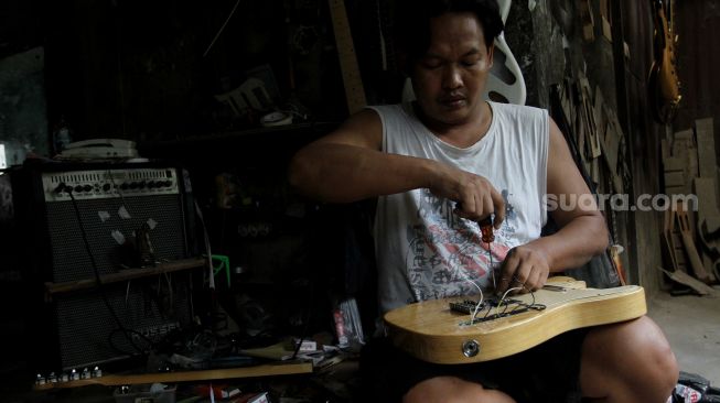 Pekerja menyelesaikan pembuatan gitar di sentra produksi dan reparasi gitar Pak Manto di Jalan Langgar II, Pejaten Timur, Pasar Minggu, Jakarta, Kamis (9/6/2022). [Suara.com/Angga Budhiyanto]