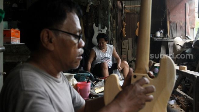 Pekerja menyelesaikan pembuatan gitar di sentra produksi dan reparasi gitar Pak Manto di Jalan Langgar II, Pejaten Timur, Pasar Minggu, Jakarta, Kamis (9/6/2022). [Suara.com/Angga Budhiyanto]