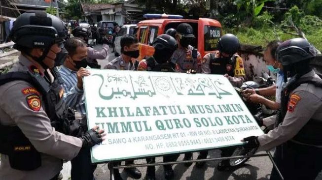Polisi menurunkan papan ormas Khilafatul Muslimin dari rumah warga. [Antara]