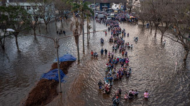 Foto udara ratusan pekerja industri kawasan pelabuhan berjalan menembus banjir limpasan air laut ke daratan atau rob yang merendam kawasan Pelabuhan Tanjung Emas Semarang, Jawa Tengah, Senin (20/6/2022).  ANTARA FOTO/Aji Styawan