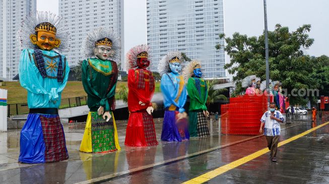 Warga melintas di depan Ondel-ondel raksasa yang terpajang di Pelataran Taman Ismail Marzuki, Jakarta Pusat, Rabu (22/6/2022). [Suara.com/Alfian Winanto]