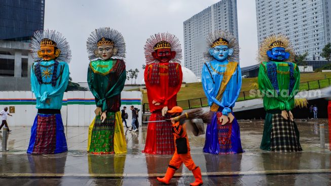 Warga melintas di depan Ondel-ondel raksasa yang terpajang di Pelataran Taman Ismail Marzuki, Jakarta Pusat, Rabu (22/6/2022). [Suara.com/Alfian Winanto]