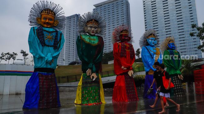 Warga melintas di depan Ondel-ondel raksasa yang terpajang di Pelataran Taman Ismail Marzuki, Jakarta Pusat, Rabu (22/6/2022). [Suara.com/Alfian Winanto]