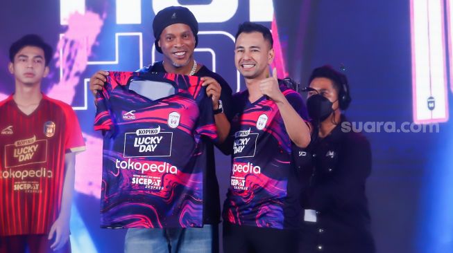 Legenda Sepak Bola Brazil, Ronaldinho (kiri) bersama Chairman RANS Nusantara FC, Raffi Ahmad (kanan) menunjukkan jersey baru untuk musim 2022-2023 di Jakarta, Jum'at (24/6/2022). [Suara.com/Alfian Winanto]