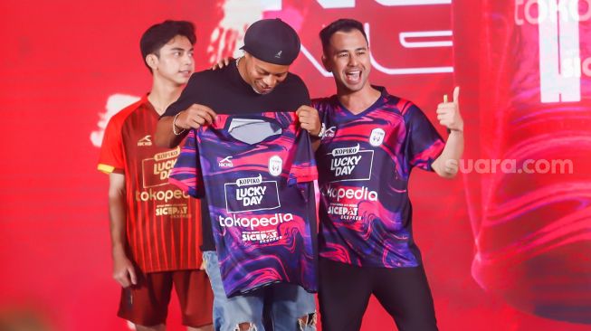 Legenda Sepak Bola Brazil, Ronaldinho (kiri) bersama Chairman RANS Nusantara FC, Raffi Ahmad (kanan) menunjukkan jersey baru untuk musim 2022-2023 di Jakarta, Jum'at (24/6/2022). [Suara.com/Alfian Winanto]