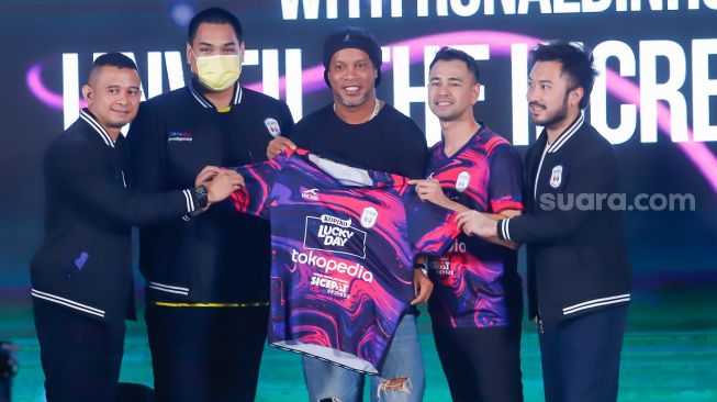 Legenda Sepak Bola Brazil, Ronaldinho (tengah) bersama Chairman RANS Nusantara FC, Raffi Ahmad (kedua kanan) dan Rudy Salim (kanan) menunjukkan jersey baru untuk musim 2022-2023 di Jakarta, Jum'at (24/6/2022). [Suara.com/Alfian Winanto]