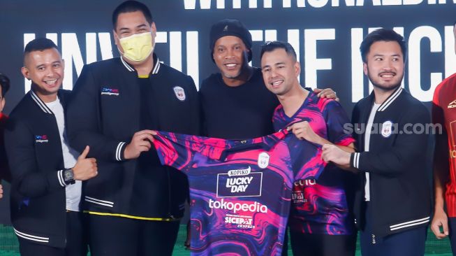 Legenda Sepak Bola Brazil, Ronaldinho (tengah) bersama Chairman RANS Nusantara FC, Raffi Ahmad (kedua kanan) dan Rudy Salim (kanan) menunjukkan jersey baru untuk musim 2022-2023 di Jakarta, Jum'at (24/6/2022). [Suara.com/Alfian Winanto]