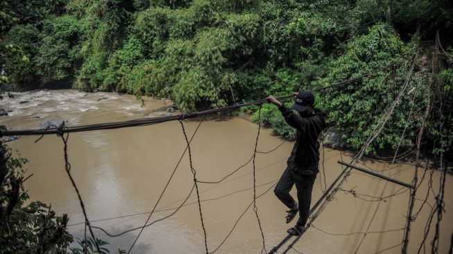 Warga menyeberangi sungai menggunakan jembatan kawat besi di Desa Salamnunggal, Kecamatan Cibeber, Kabupaten Cianjur, Jawa Barat, Sabtu (25/6/2022). [ANTARA FOTO/Raisan Al Farisi/rwa]