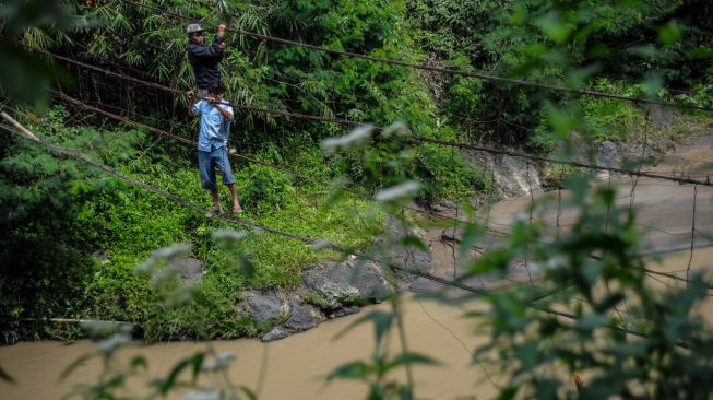 Warga menyeberangi sungai dengan menggunakan jembatan kawat besi di Desa Salamnunggal, Kecamatan Cibeber, Kabupaten Cianjur, Jawa Barat, Sabtu (25/6/2022). [ANTARA FOTO/Raisan Al Farisi/rwa]