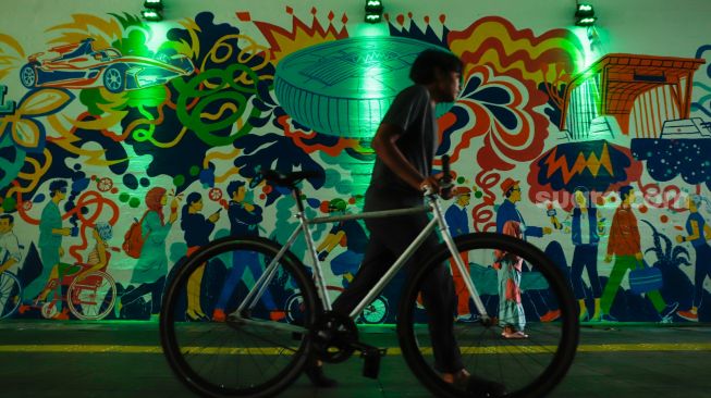 Warga melintas dengan latar belakang mural bertema Jakarta Kota Global di Terowongan Kendal, Jakarta Pusat, Senin (27/6/2022). [Suara.com/Alfian Winanto]