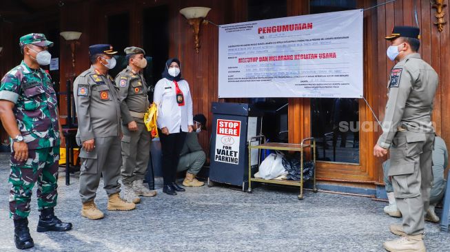 Petugas Satuan Polisi Pamong Praja (Satpol PP) saat memasang spanduk berisi informasi penutupan dan penyegelan outlet Holywings Epicentrum di Kuningan, Jakarta Selatan, Selasa (28/6/2022). [Suara.com/Alfian Winanto]