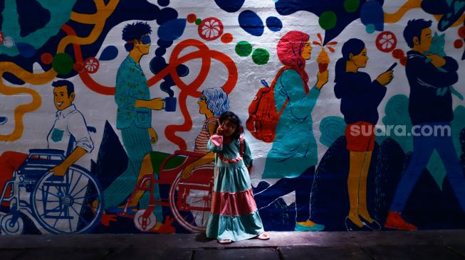 Anak-anak bermain dengan latar belakang mural bertema Jakarta Kota Global di Terowongan Kendal, Jakarta Pusat, Senin (27/6/2022). [Suara.com/Alfian Winanto]