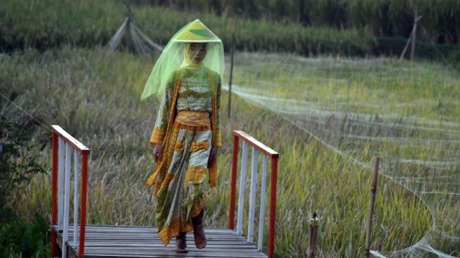 Seorang model mengenakan busana dari bahan kain perca saat peragaan busana di tengah persawahan di kampung tematik Agro Eduwisata Organik Mulyaharja, Kota Bogor, Jawa Barat, Selasa (5/7/2022).  ANTARA FOTO/Arif Firmansyah
