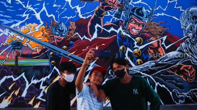 Warga berswafoto di dekat mural kolaborasi bergambar Thor di Terowongan Kendal, Jakarta Pusat, Selasa (5/7/2022). [Suara.com/Alfian Winanto]