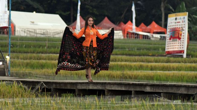 Seorang model mengenakan busana dari bahan kain perca saat peragaan busana di tengah persawahan di kampung tematik Agro Eduwisata Organik Mulyaharja, Kota Bogor, Jawa Barat, Selasa (5/7/2022).  ANTARA FOTO/Arif Firmansyah
