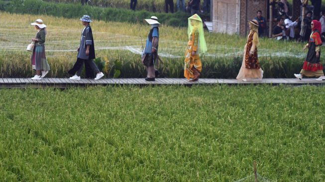 Seorang model mengenakan busana dari bahan kain perca saat peragaan busana di tengah persawahan di kampung tematik Agro Eduwisata Organik Mulyaharja, Kota Bogor, Jawa Barat, Selasa (5/7/2022).  ANTARA FOTO/Arif Firmansyah
